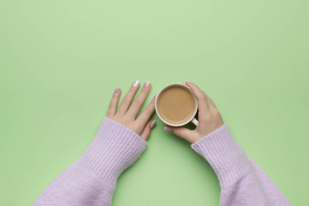 Female hands in a purple sweater with a cup of coffee on a green background. The concept of drinking a popular drink. Flat lay. - Foto, immagini