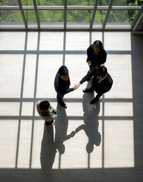 Business partners shaking hands in the modern office. Standing near the window while the sunlight shines on them. There is a shadow on the wooden floor - Photo, Image