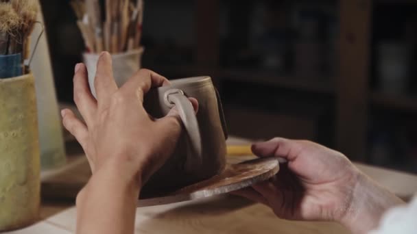 Young woman pressing the piece of clay to an edge of the handle and a cup - Materiaali, video