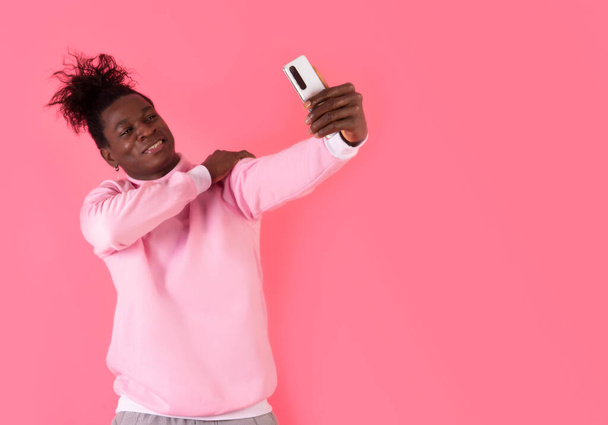 Studio picture of a young afro man talking a selfie looking happy and confident, in a studio shot and pink mood - Photo, Image