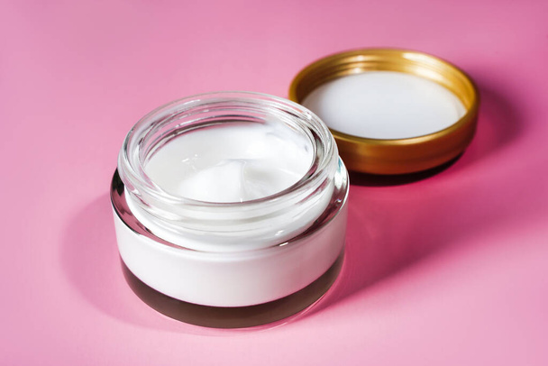 Crema blanca antiarrugas hidratante cosmética en frasco de vidrio sobre fondo rosa - Foto, Imagen