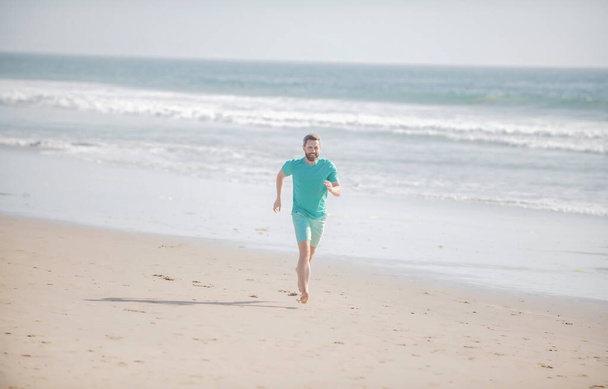 Man running on beach. Jogging on a sandy beach near sea or ocean. - Фото, изображение