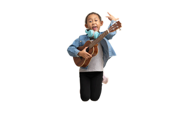 Happy Asian child girl jumping play ukulele, isolate on white background. - Photo, image