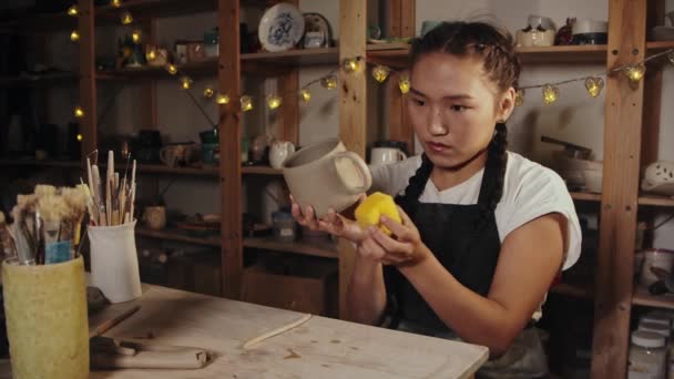 Young woman potter smoothing out the clay cup using a sponge - Metraje, vídeo