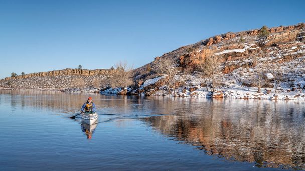 senior male wearing life jacket  is paddling expedition canoe in witer scenery of Horsetooth Reservoir in northern Colorado - Фото, зображення