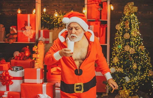 Santa picking cookie and glass of milk at home. Greeting Christmas card. Milk and gingerbread cookie for Santa against Christmas light background. - Φωτογραφία, εικόνα