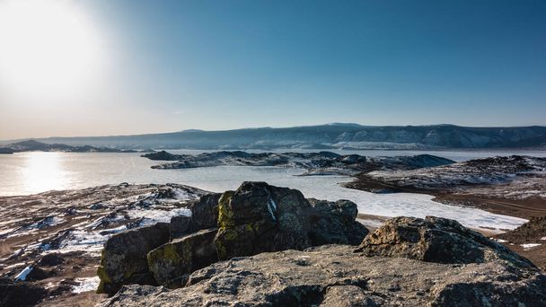 Winter Siberian landscape. The sun is shining in the blue sky. Glare on the ice of a frozen lake. Picturesque rocks on a snow-covered ground. Baikal - Foto, Imagem