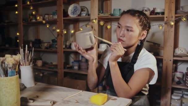 若い女性の陶芸家は、ぬれたブラシを使用して粘土カップを平滑化 - 映像、動画