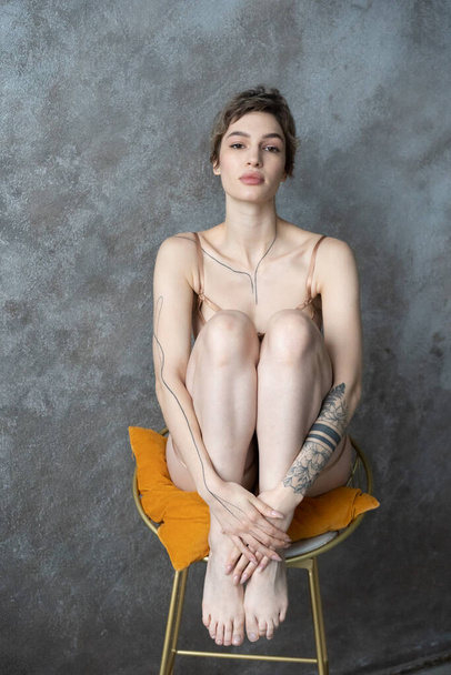 young beautiful woman sits on a chair with her legs tucked in underwear - Foto, afbeelding