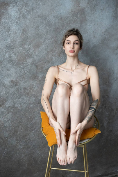 young beautiful woman sits on a chair with her legs tucked in underwear - Foto, Imagem