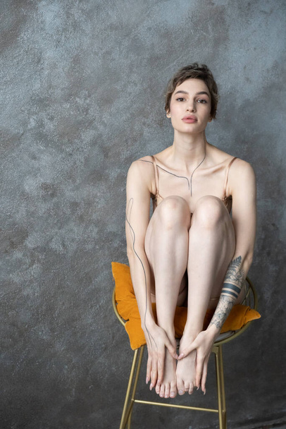 young beautiful woman sits on a chair with her legs tucked in underwear - Photo, image
