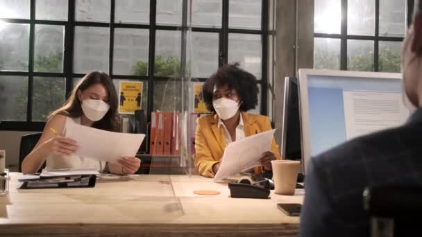Yeni normal ofiste çalışan yüz maskeli iki bayan iş arkadaşı. COVID-19 Bölünme, işyeri ofisi, salgın hastalıkların önlenmesi için sosyal uzaklık. - Video, Çekim