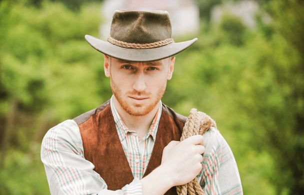 Guy cowboy. Owner of ranch. Farm worker and farming concept. Cowboy with lasso rope on green background. Handsome man in cowboy hat and rustic style outfit. - Фото, изображение