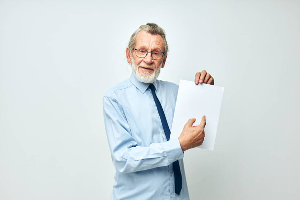 Senior grey-haired man holding documents with a sheet of paper light background - Fotografie, Obrázek