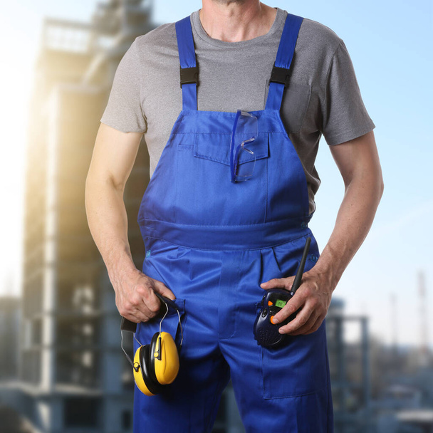 Mannelijke werknemer met beschermende oorkappen en radiozender op de bouwplaats - Foto, afbeelding