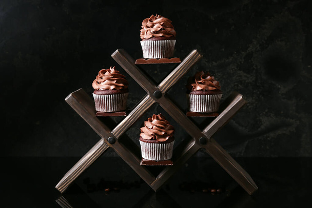 Soporte de madera con sabrosos cupcakes de chocolate sobre fondo oscuro - Foto, Imagen