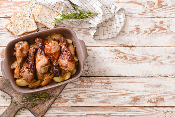 Baking dish with tasty cooked chicken drumsticks and potatoes on table - Valokuva, kuva