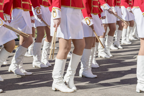 赤と白の儀式的なスーツの若い女の子の大規模なグループは、街の通りに形成に行進します。太鼓の祭りの行列。サイドビュー. - 写真・画像