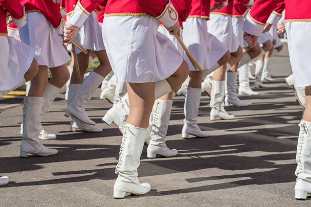 Large group of young girls in red and white ceremonial suits march in formation on city street. Festive procession of drummers. Side view. - 写真・画像