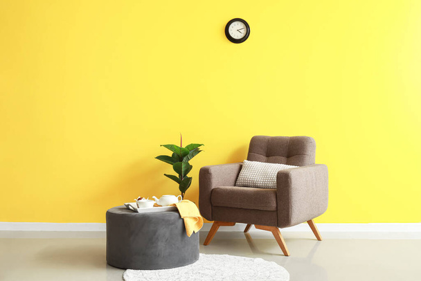 Pouf with breakfast, houseplant and soft armchair near yellow wall - Фото, зображення