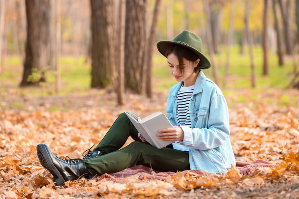 Young woman reading interesting book on plaid in autumn park - Fotoğraf, Görsel