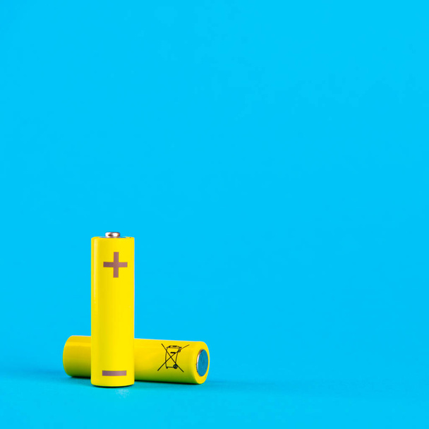 Two yellow AA alkaline batteries or NiMH rechargeable batteries on a blue background with space for text. Power elements on a blue background. - Foto, Bild
