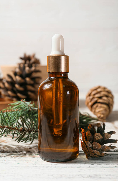 Bottle of essential oil, fir branch and pine cones on light wooden background, closeup - Fotó, kép
