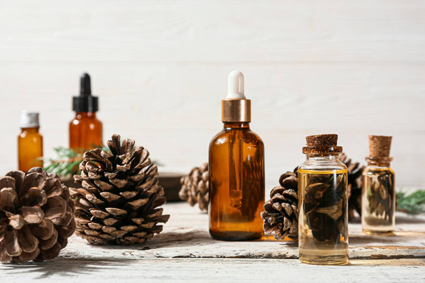Bottles of essential oil and pine cones on light wooden background - Foto, Imagem
