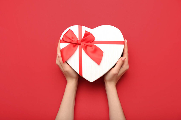 Female hands with gift box for Valentine's Day on red background - Фото, изображение