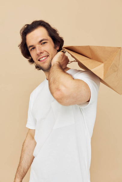 man in a white T-shirt with paper bag beige background - Foto, imagen