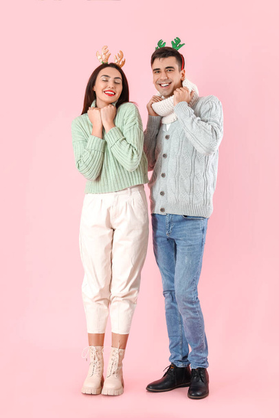 Happy young couple in warm sweaters and with deer horns on color background - Фото, изображение