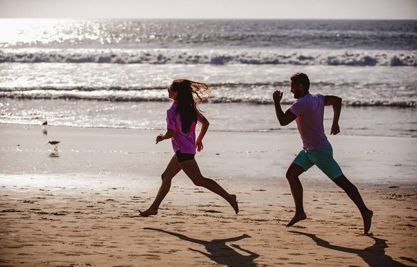 Desporto e estilo de vida saudável, amigos a correr ao pôr do sol na praia. Casal silhueta correndo na praia. - Foto, Imagem