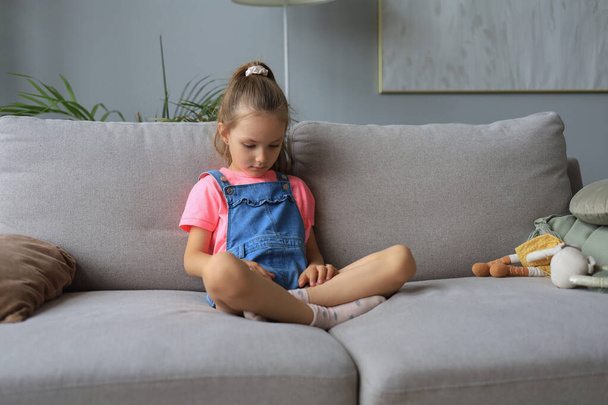 Sad little girl sitting on sofa alone at home - Foto, afbeelding