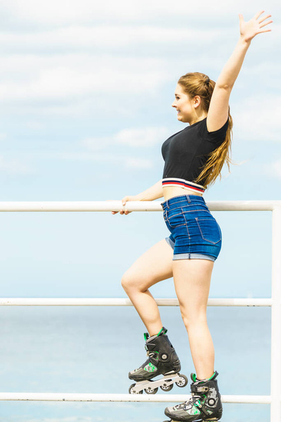 Attractive young woman wearing roller skates relaxing after ride. Fit female having fun during summer time on sea coast. - Foto, immagini