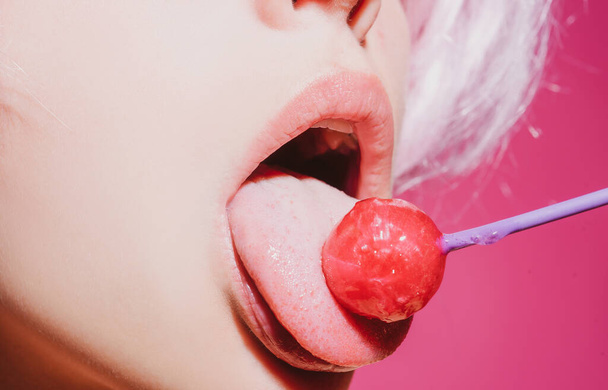 Licking candy. Lollipop model. Woman lips sucking a candy. Glamor sensual model with red lips eat sweats lolly pop. - Foto, afbeelding