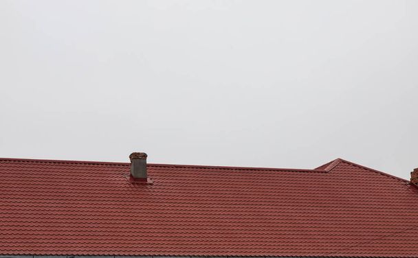 Le toit de la maison est fait de tuiles métalliques rouges, une belle grande cheminée. - Photo, image