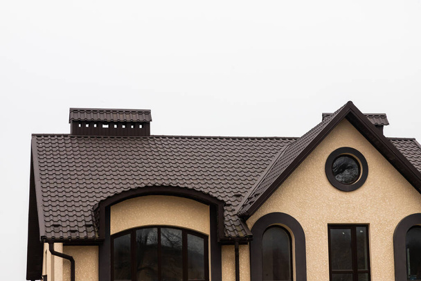 Das Dach des Hauses besteht aus roten Metallziegeln, ein schöner großer Schornstein. - Foto, Bild