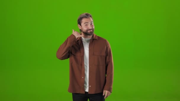 Bearded man doing phone gesture over green background - Filmati, video