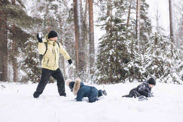 Father and sons having fun snowball fight together in winter forest. Happy children playing in snow outdoors. Christmas holidays, New year family vacation. Brothers in warm clothes walking in cold day - Photo, Image