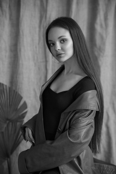 Black and white fashion portrait of a beautiful girl with natural makeup in a leather coat in the studio. - Zdjęcie, obraz