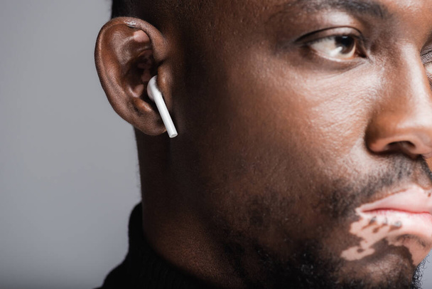 close up view of cropped african american man with vitiligo listening music in earphone isolated on grey - Photo, image