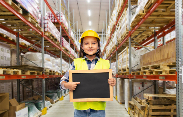little girl in helmet with chalkboard at warehouse - Фото, изображение