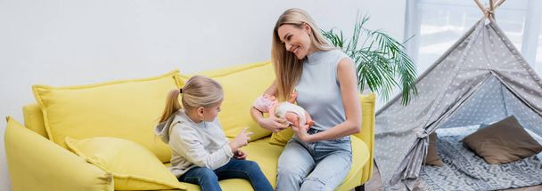 Positive woman holding doll near kid on couch at home, banner  - Foto, immagini