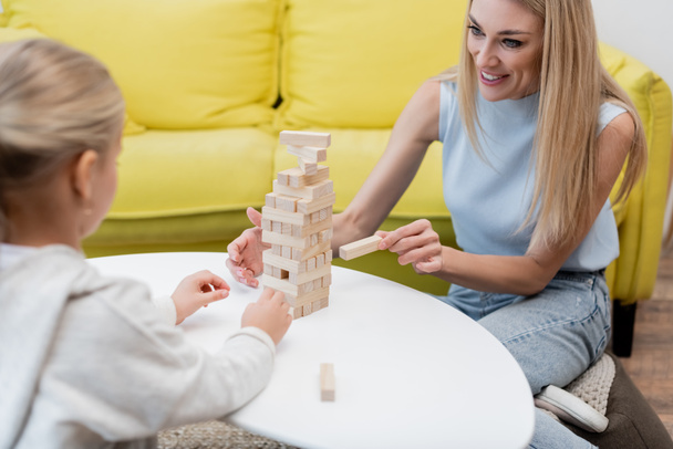 Woman playing wood blocks game with blurred daughter at home  - Φωτογραφία, εικόνα