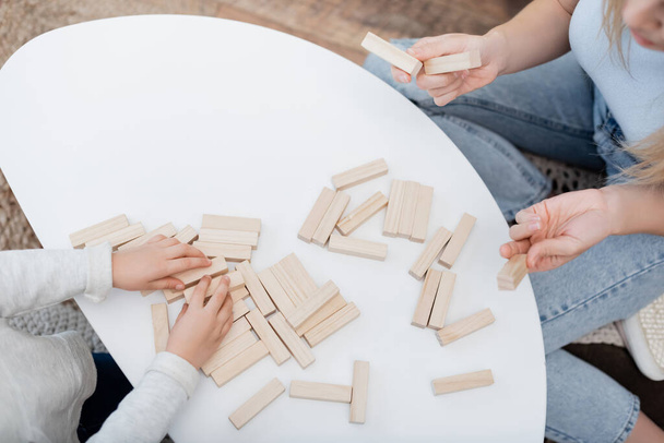 Cropped view of mother holding wooden blocks near kid and coffee table at home  - Foto, Bild