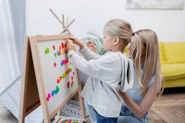 Child fastening colorful magnets on easel near parent at home  - Photo, Image