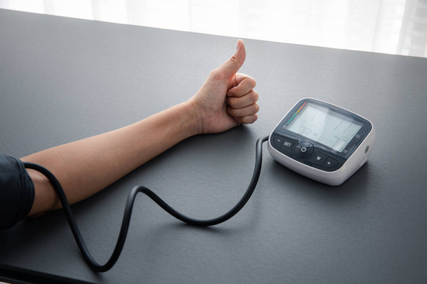 Pulgar hacia arriba en la presión arterial propia y la medición de la frecuencia cardíaca con la máquina de monitor de presión arterial, la atención médica y el concepto médico - Foto, Imagen