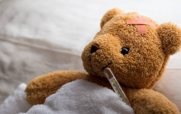 Teddy bear lying sick in hospital bed with with thermometer and plaster. Healthcare and medical concept. - Photo, Image