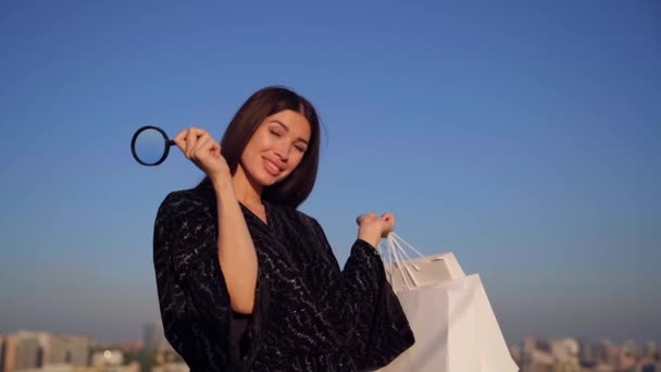 Ευτυχισμένο κορίτσι αίγλη με μεγεθυντικό φακό και τσάντες ψώνια - Πλάνα, βίντεο