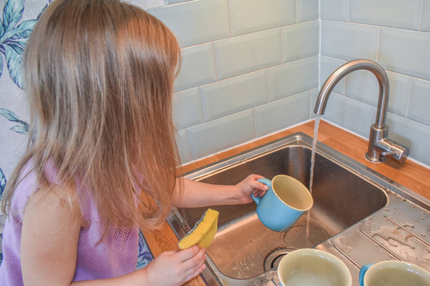 a child washes mugs in the sink photo without a filter - Foto, Bild
